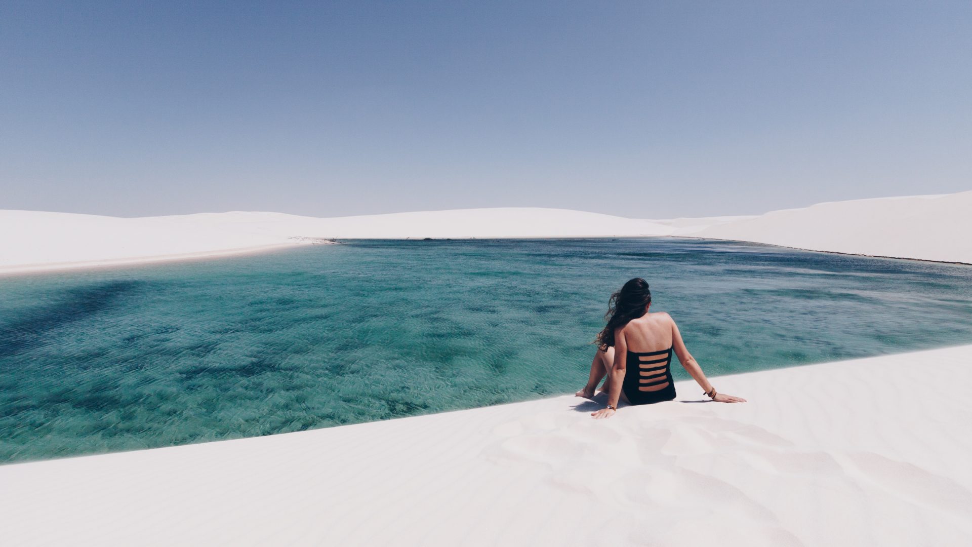 mujer sentada en la cima de una duna observando la laguna que se formó en el desierto.