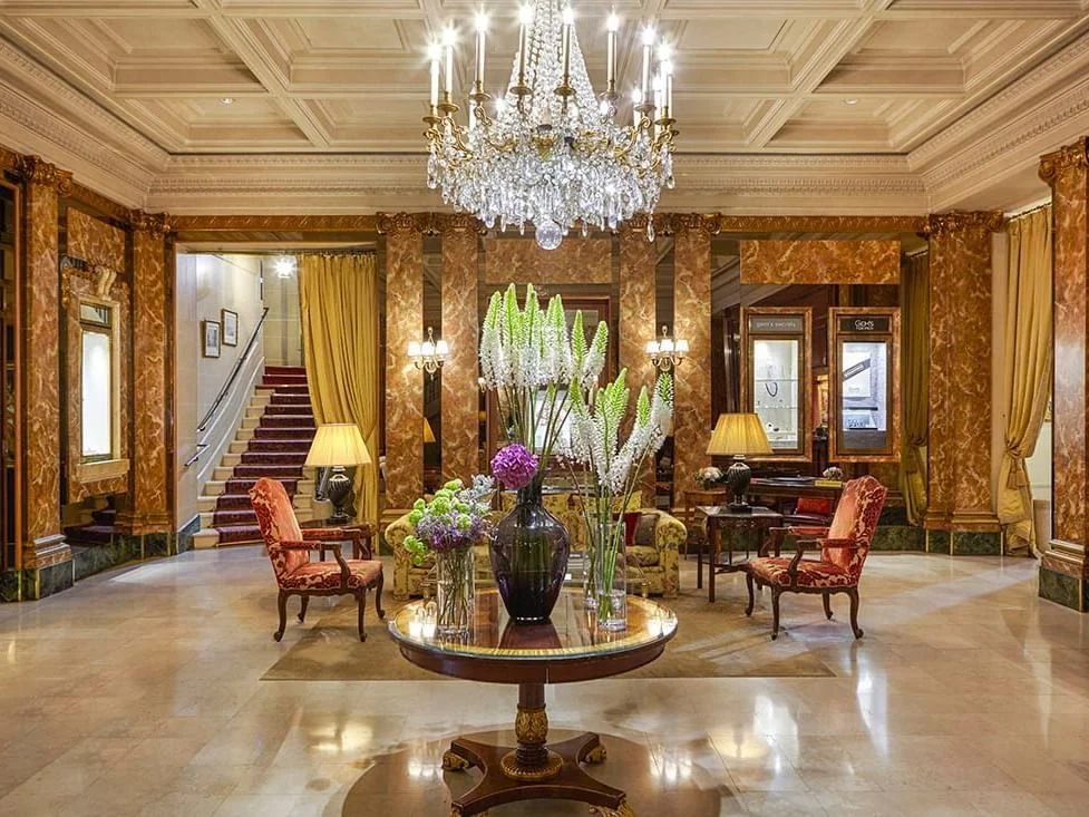 lobby del hotel westminster en parís con un candelabro de cristal colgando del techo, una sala de estar y una mesa con floreros.